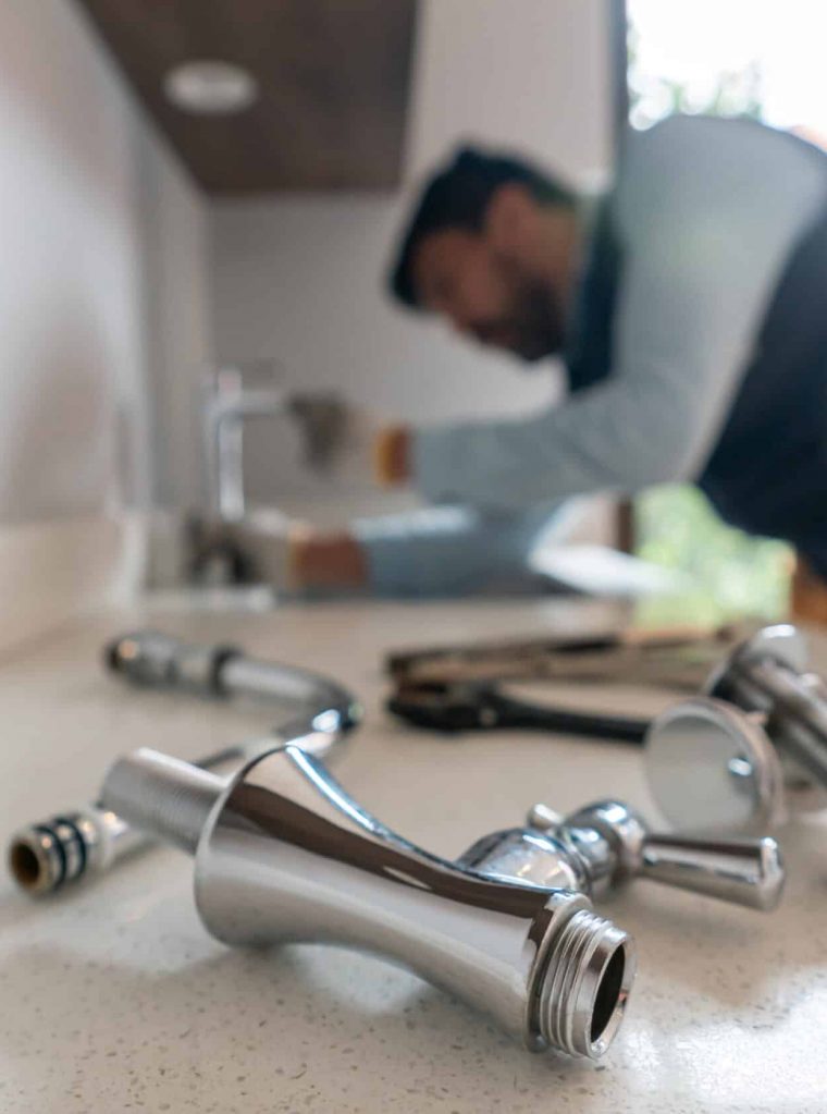 Plumber fixing a leak in the kitchen sink of a house Latin American plumber fixing a leak in the kitchen sink of a house - focus on his tools