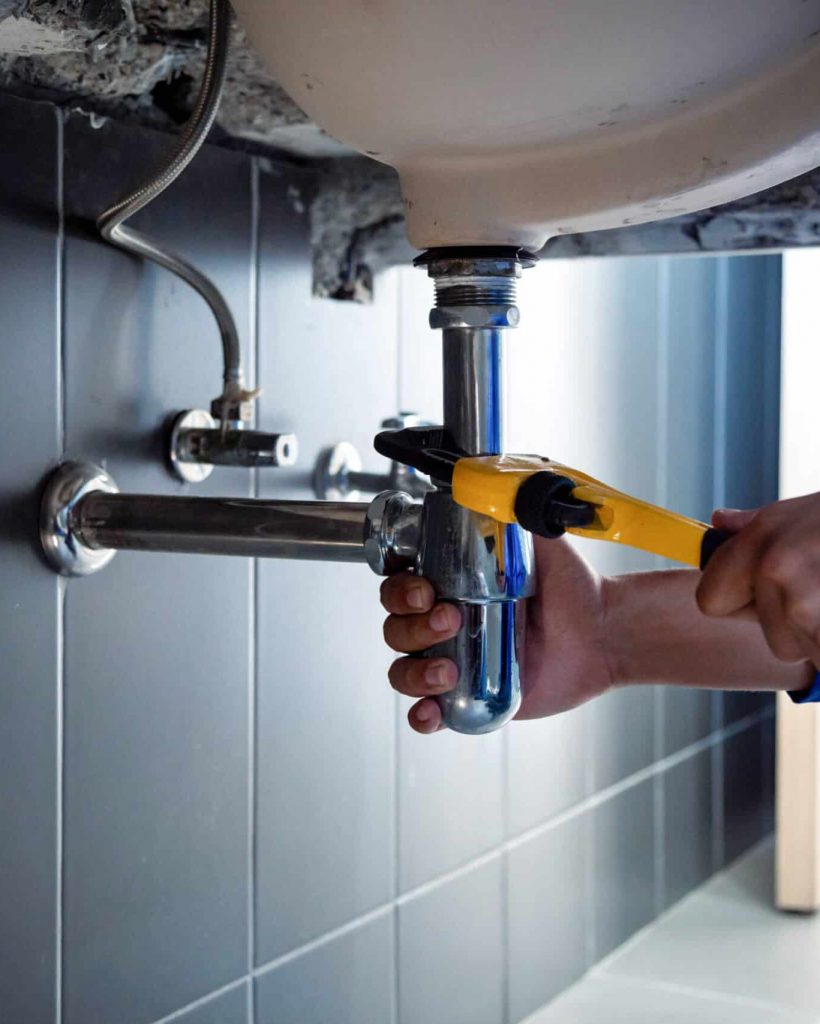 Plumber fixing white sink pipe with adjustable wrench. Plumber fixing white sink pipe with adjustable wrench.